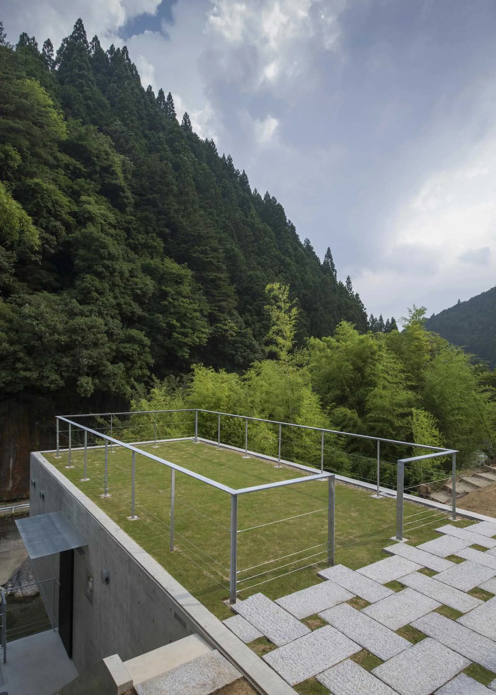 Concrete exterior featuring a green space with a metal railing and stone walkway.