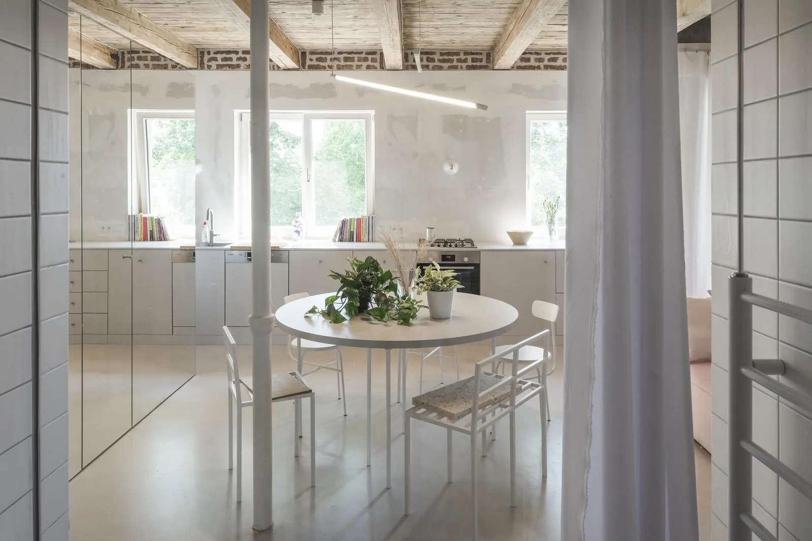 A minimalist kitchen and dining area with a round table, chairs, and plants.