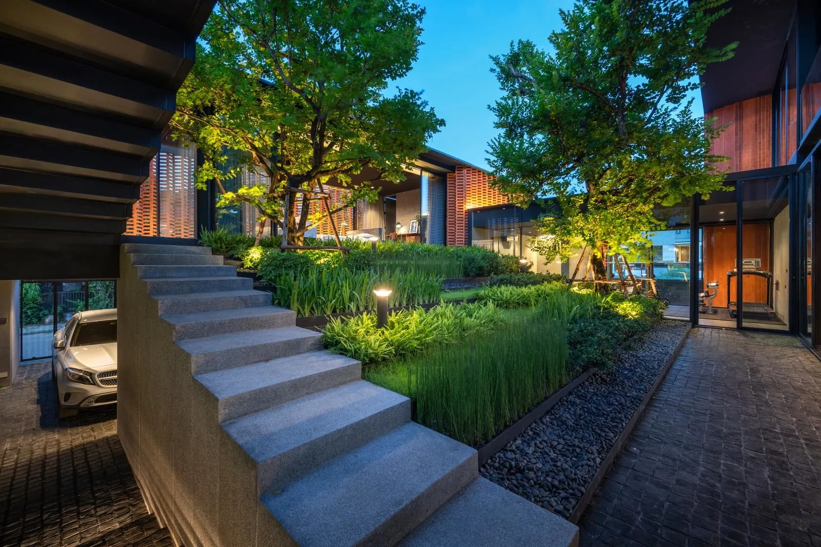 Modern residential entry with concrete steps and illuminated greenery at dusk.