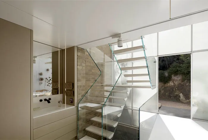 Modern residential interior featuring a glass and wooden staircase with a large window.