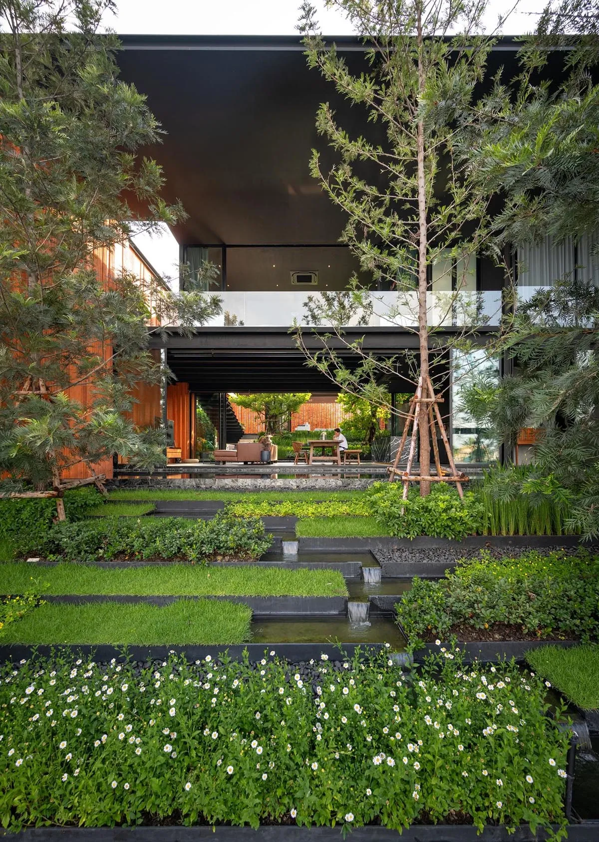 A modern house featuring a concrete exterior with lush landscaping and a water feature.