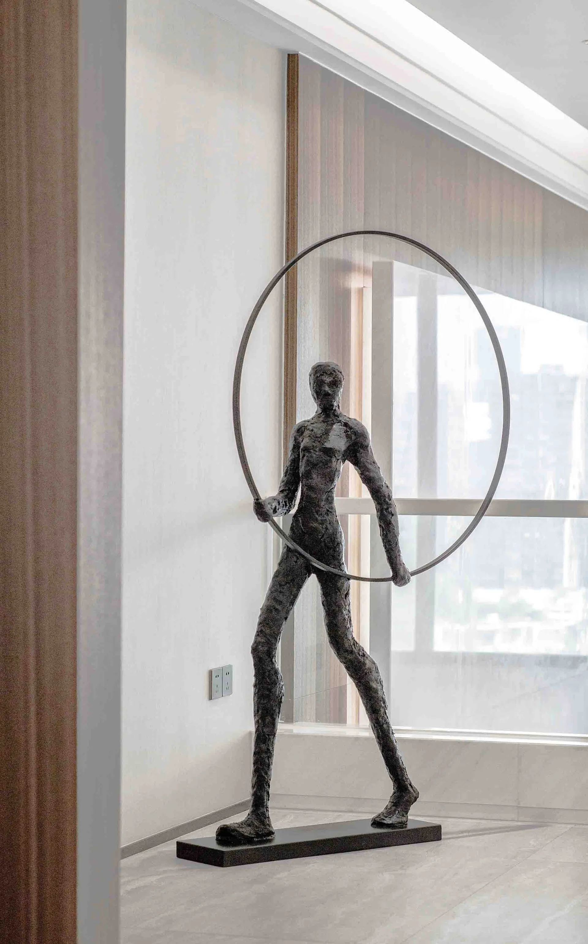 A modern metal sculpture featuring a humanoid figure holding a circular ring.