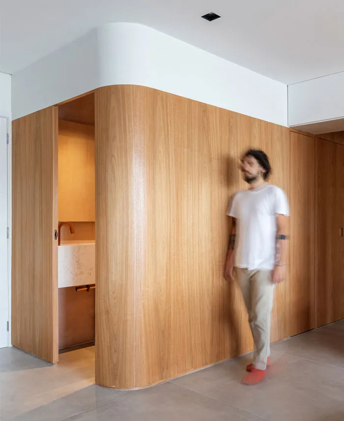 A modern minimalist interior featuring wood paneling, with a person walking in front of a curved wooden wall.