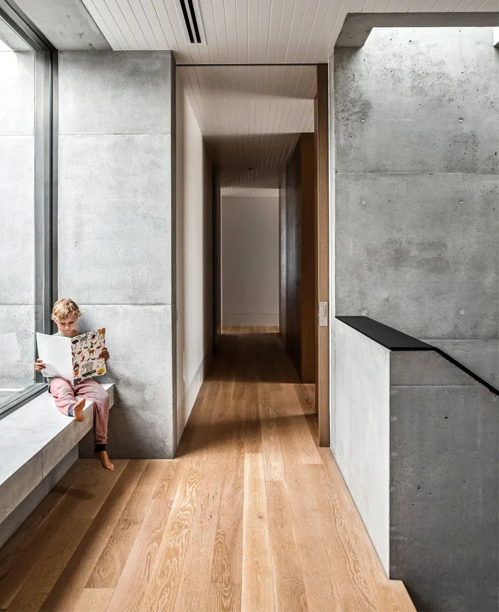 A modern living space with concrete walls and wooden flooring, featuring a child reading.