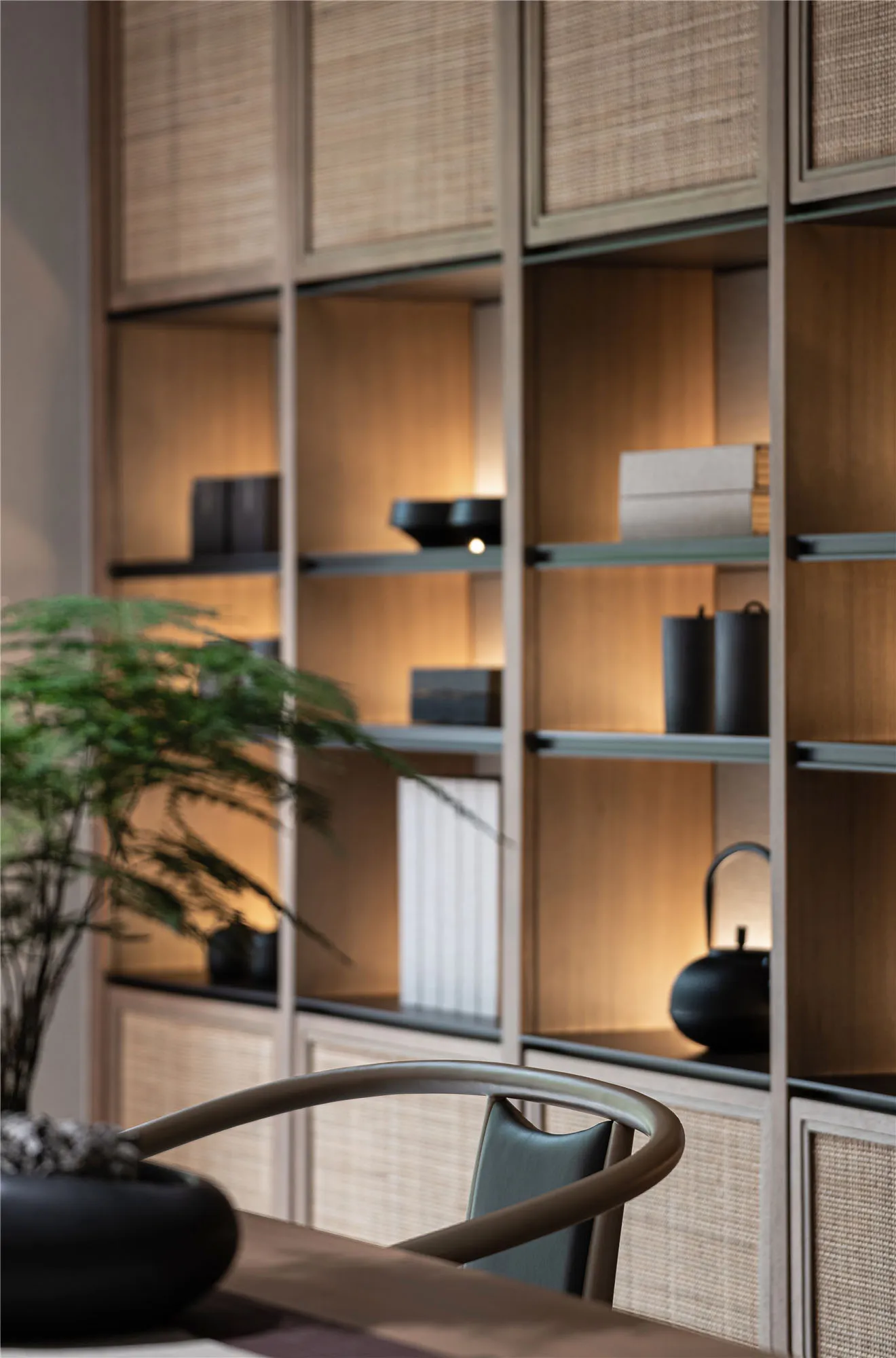 Minimalist interior design featuring a wooden shelving unit with books, plants, and decorative objects.