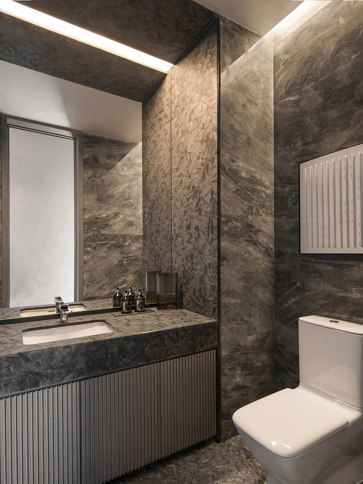 Modern bathroom featuring marble walls and flooring with a sleek vanity sink and white toilet.