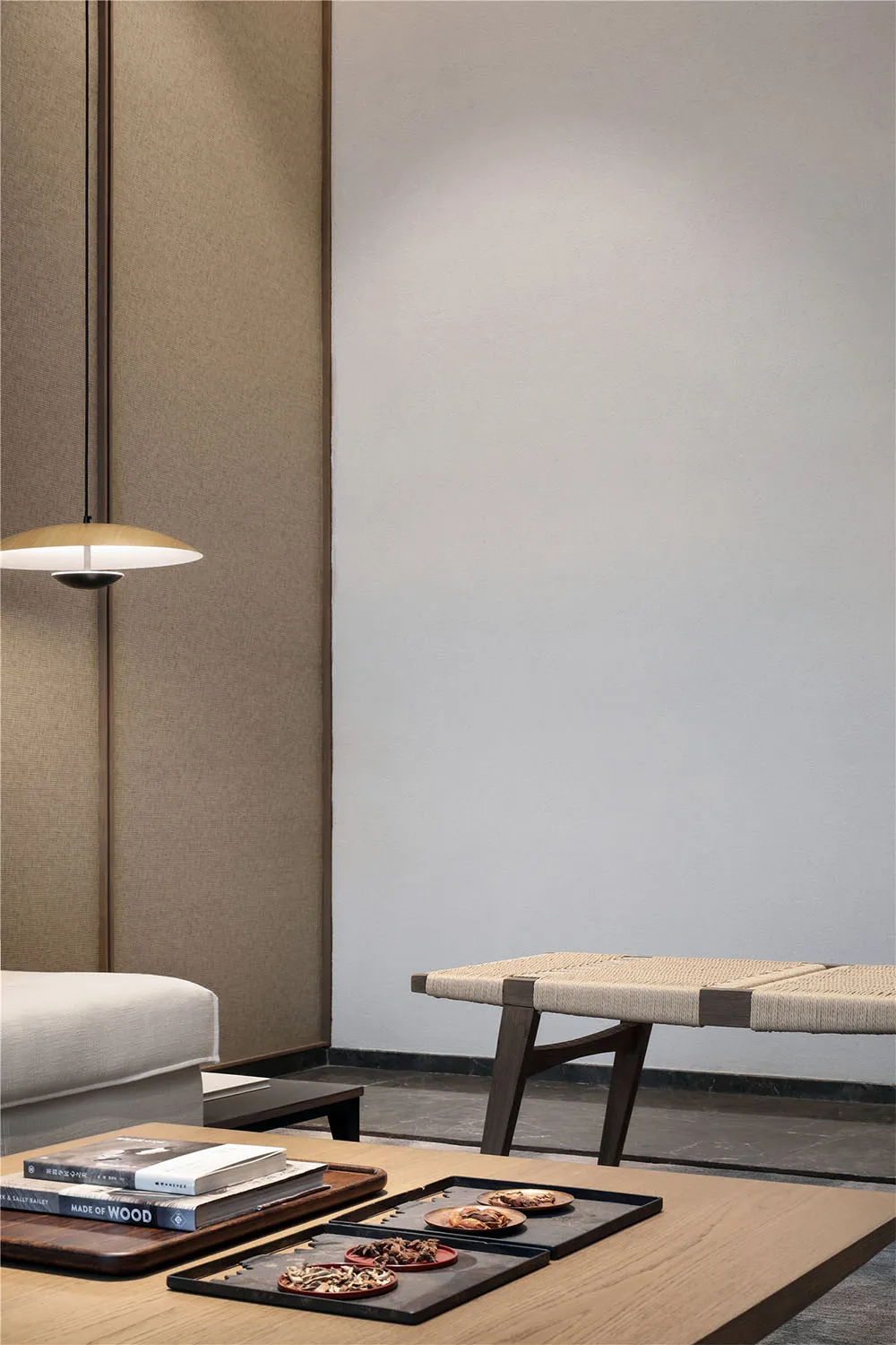 A modern living room featuring a wooden table with rope woven seat, a pendant light, and a minimalist aesthetic