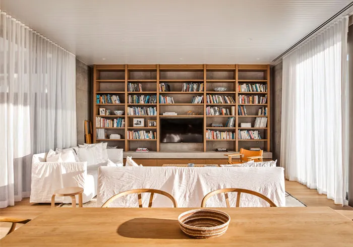 Modern living room with wooden furniture, white curtains, and a large bookshelf.