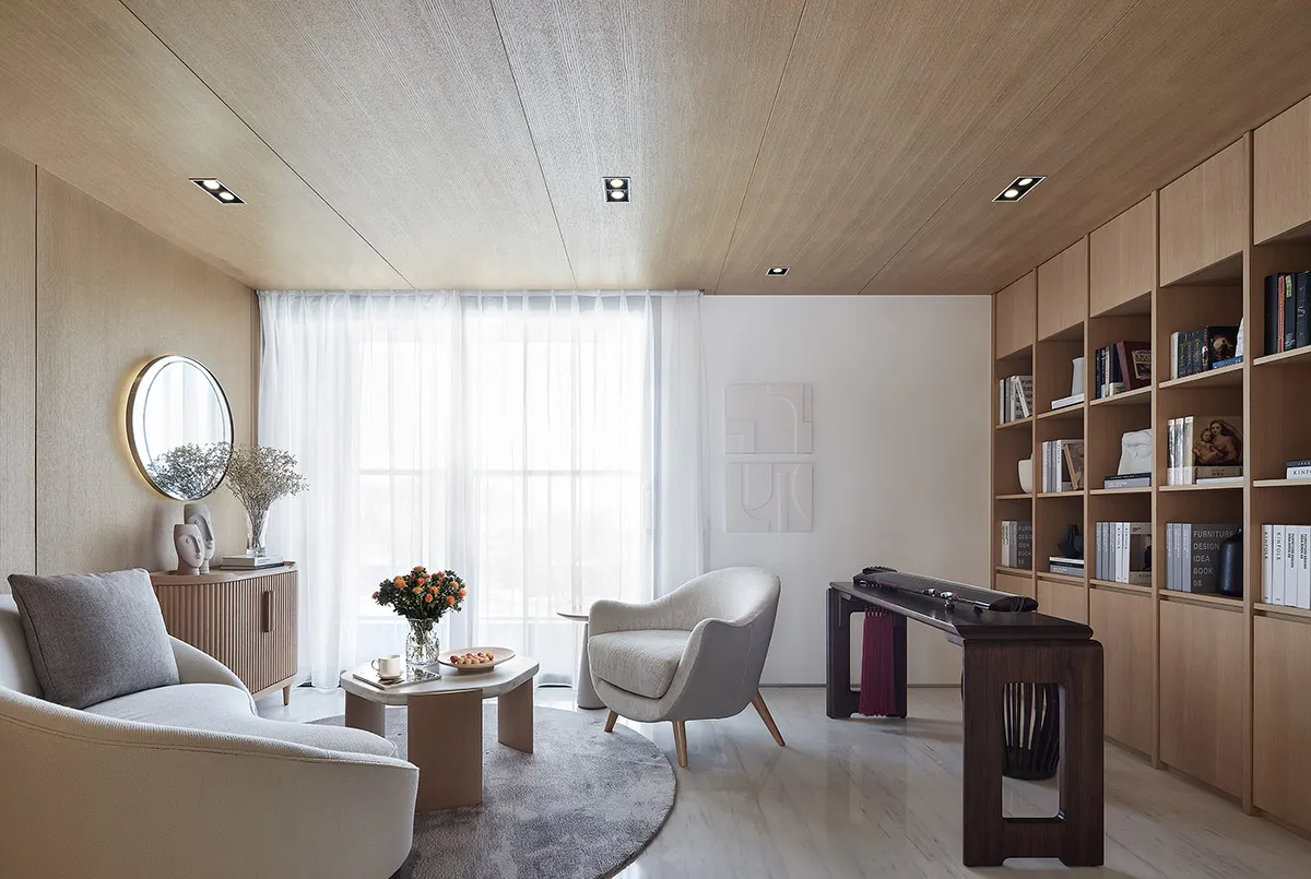 Modern living room with wooden walls and furniture, featuring a round table, armchair, and bookshelf.