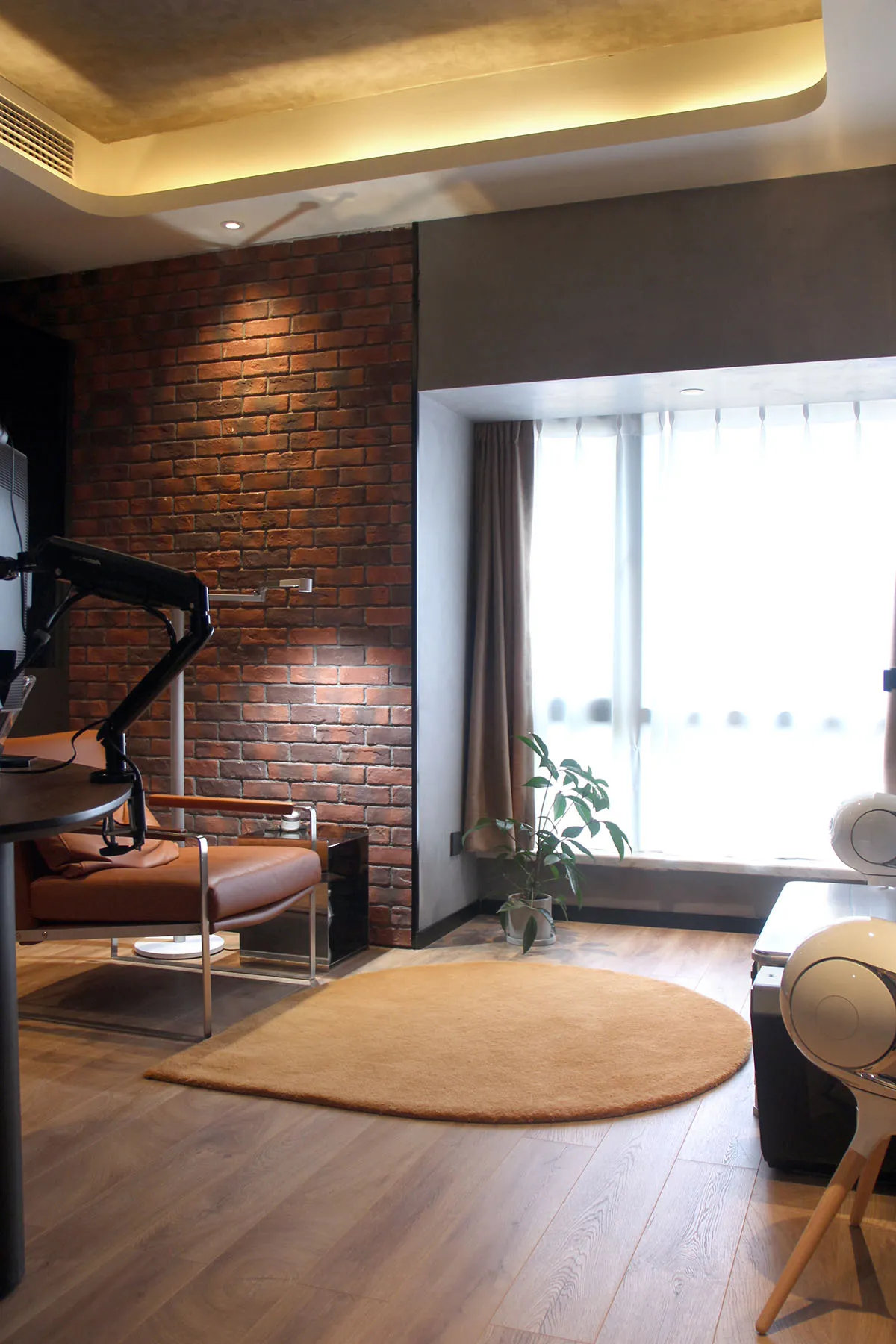 Modern living room with a brick accent wall, wooden floor, and a large window.