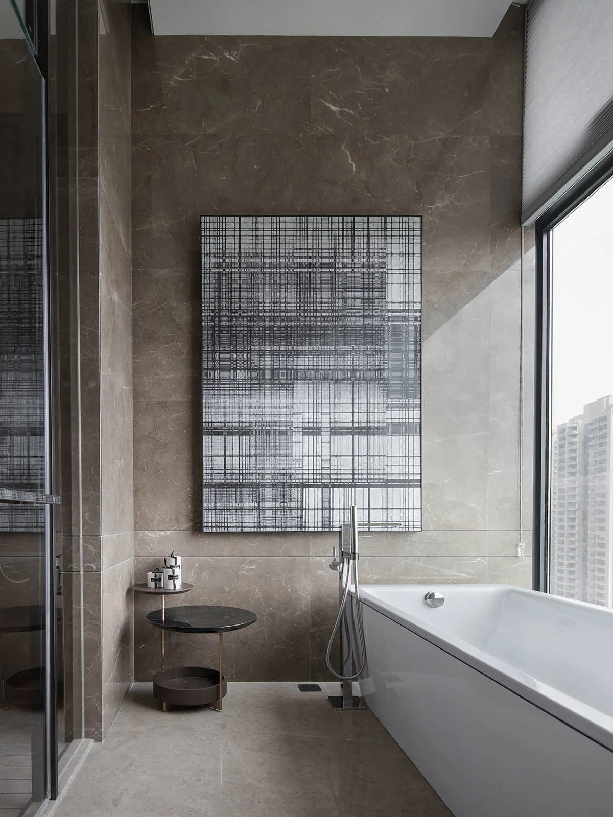 Modern bathroom featuring a marble wall and floor with a white bathtub and an abstract black and white geometric wall art.
