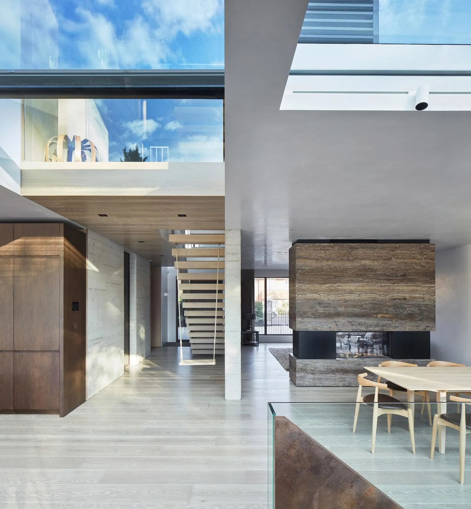 Modern residential interior featuring wood floors, glass walls, metal accents, and marble fireplace.