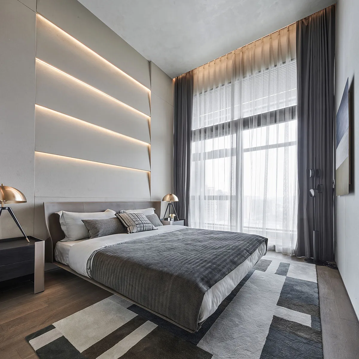 A minimalist bedroom with a gray floating bed, illuminated wall panel, and large windows with dark curtains.