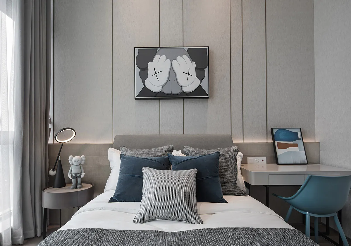 A minimalist bedroom with a grey bed, black and white accents, and a desk with a blue chair.