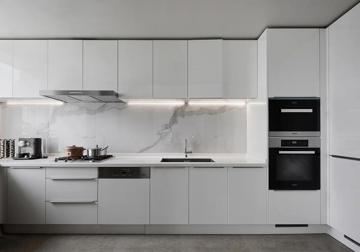 A sleek, modern kitchen with white marble countertops, white cabinets, and stainless steel appliances.