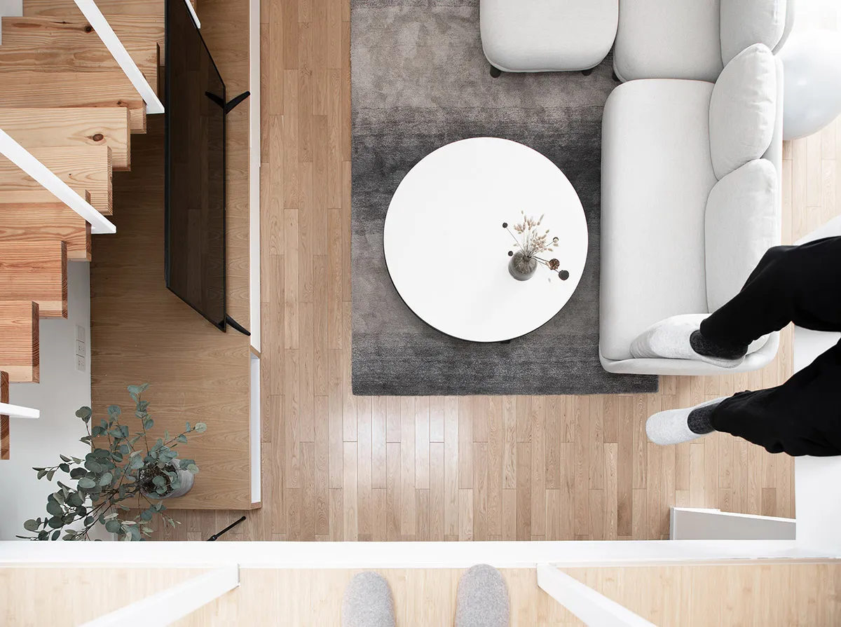 Modern minimalist living room with white furniture, wooden floors, and a circular coffee table.