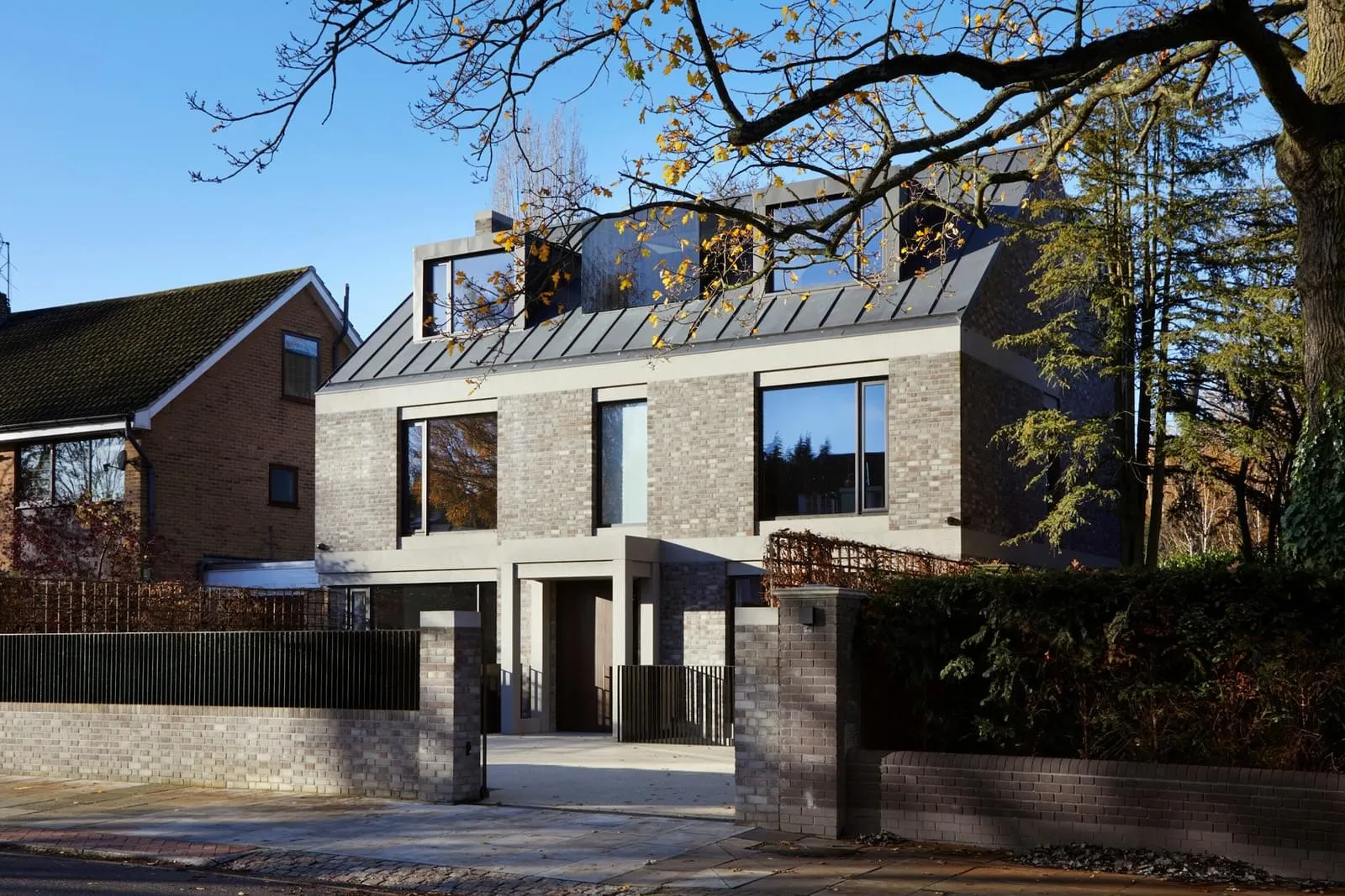 Modern brick and concrete exterior of a house with large windows and a metal roof.