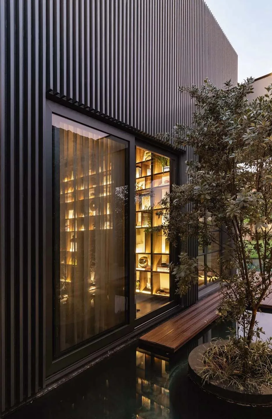 Modern minimalist library with black metal siding and a glass wall overlooks a tranquil poolside.