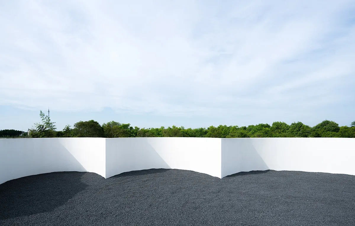 A minimalist outdoor space with white walls and gravel ground.