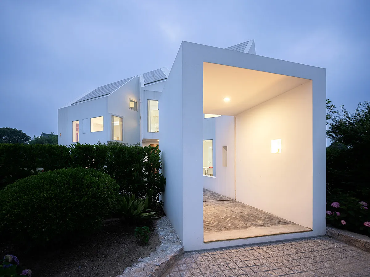 A modern house with a white exterior, concrete walls, wooden accents, and strategic lighting during twilight