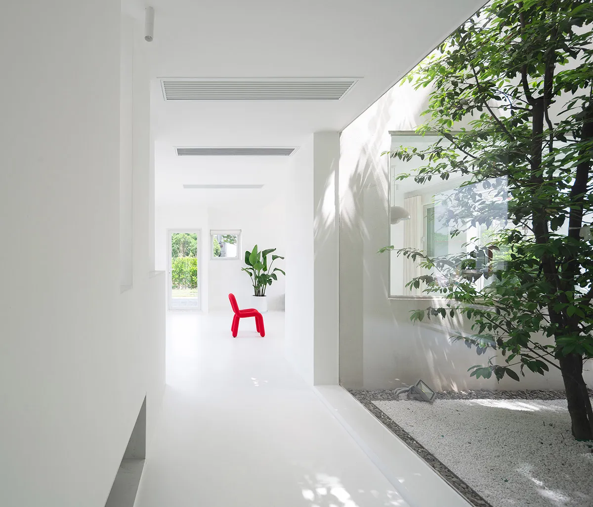 Minimalist, white, concrete interior space with modern, red chair and large window.
