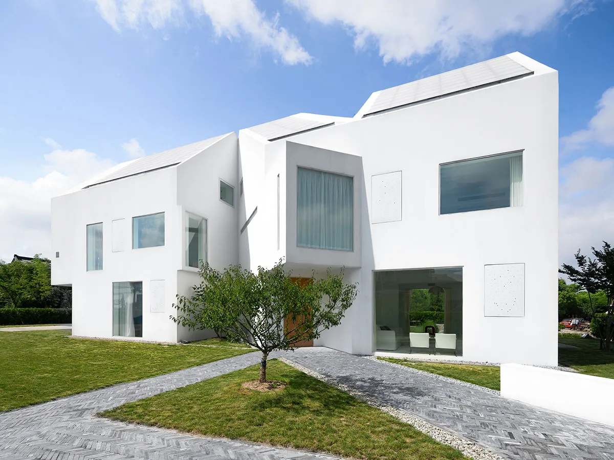 一座現代住宅建築外牆全塗白色,搭配大型玻璃窗與屋頂太陽能板。