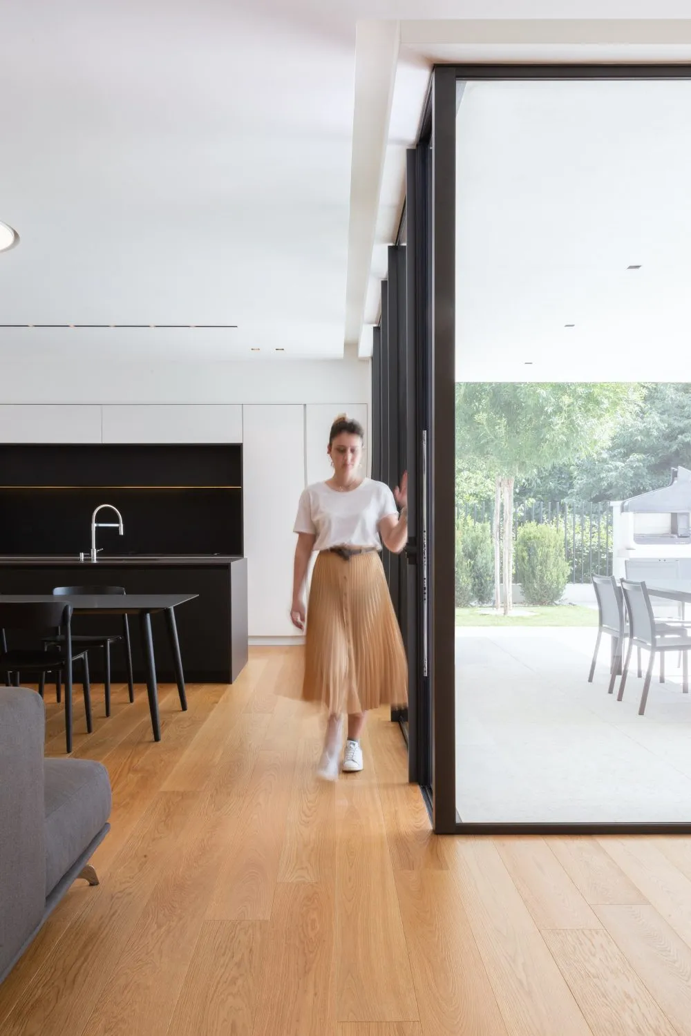 A modern residential kitchen with hardwood flooring, featuring sleek black cabinetry and a spacious dining area leading to an