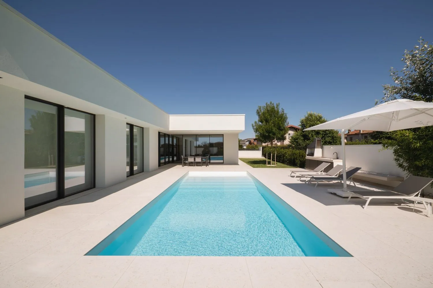 Sophisticated minimalist residential exterior featuring a clean white poolside area with concrete and glass elements.