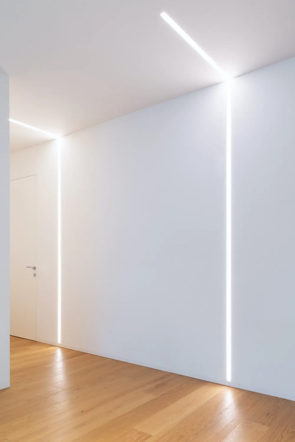 A minimalist white interior design featuring white walls, wood flooring, and linear lighting fixtures.