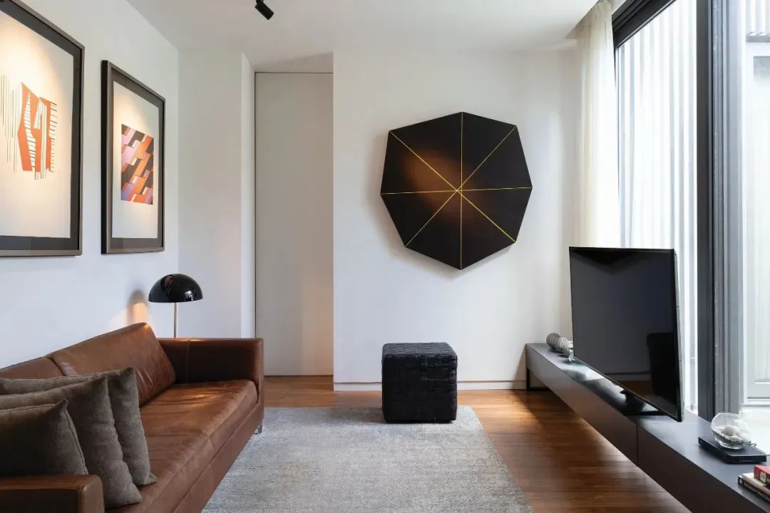 A modern living room featuring a brown leather sofa, a black geometric art piece on the wall, and a television on a floating 