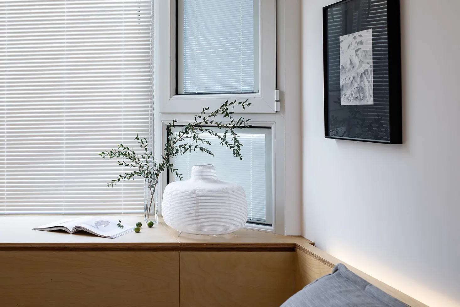 A minimalist interior design featuring wooden accents, a white vase, and greenery.