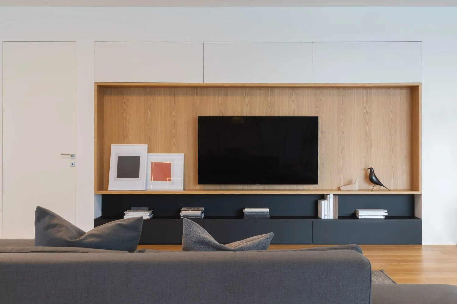 Modern living room featuring wooden shelves, a black television, and gray furniture.