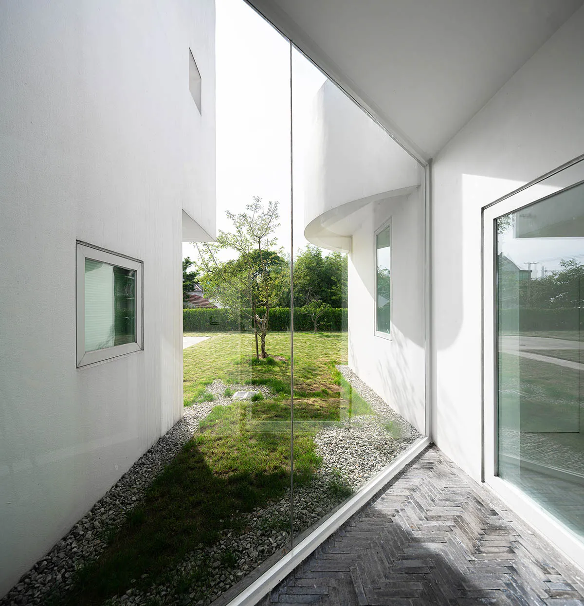 Modern minimalist house exterior with white walls, glass windows, and gravel pathway.