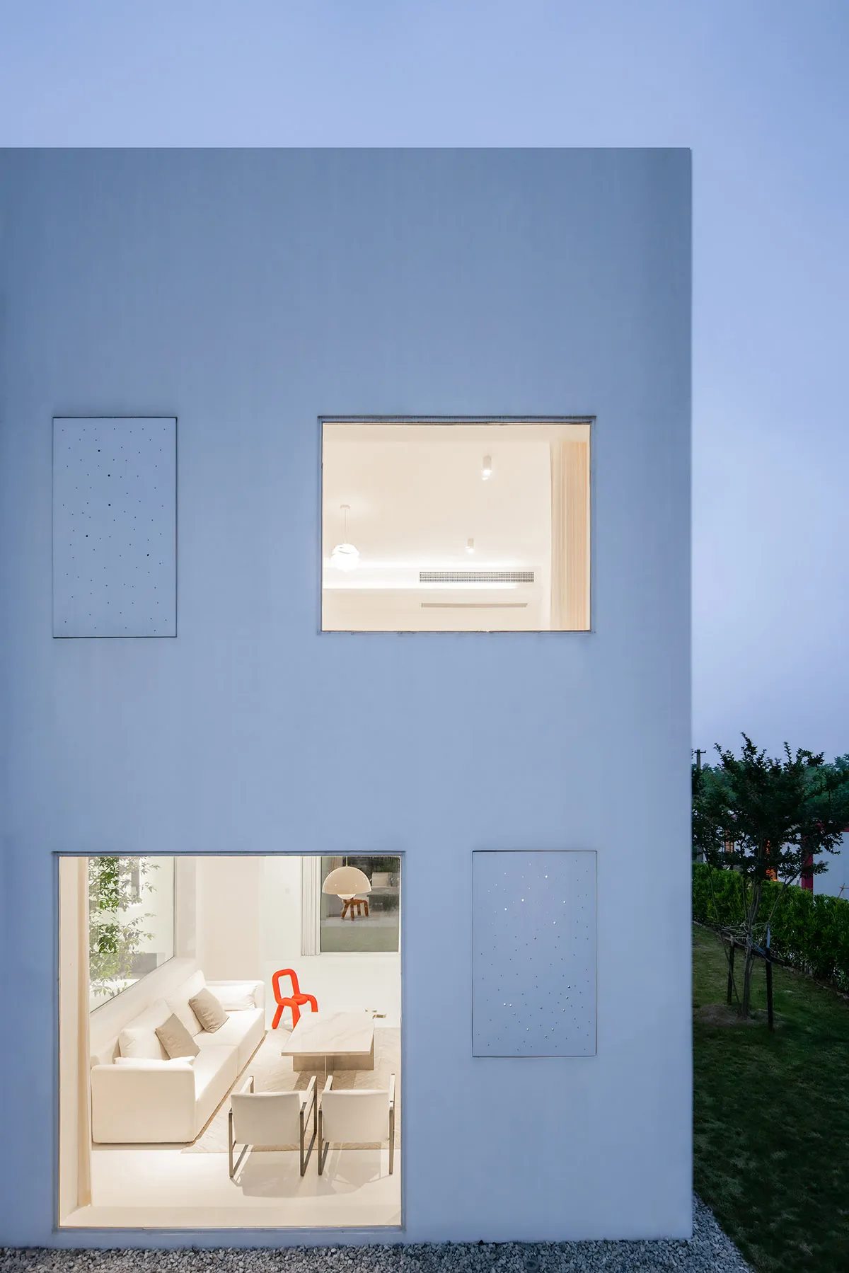 A modern residential exterior featuring a white-painted living room viewed through a window.