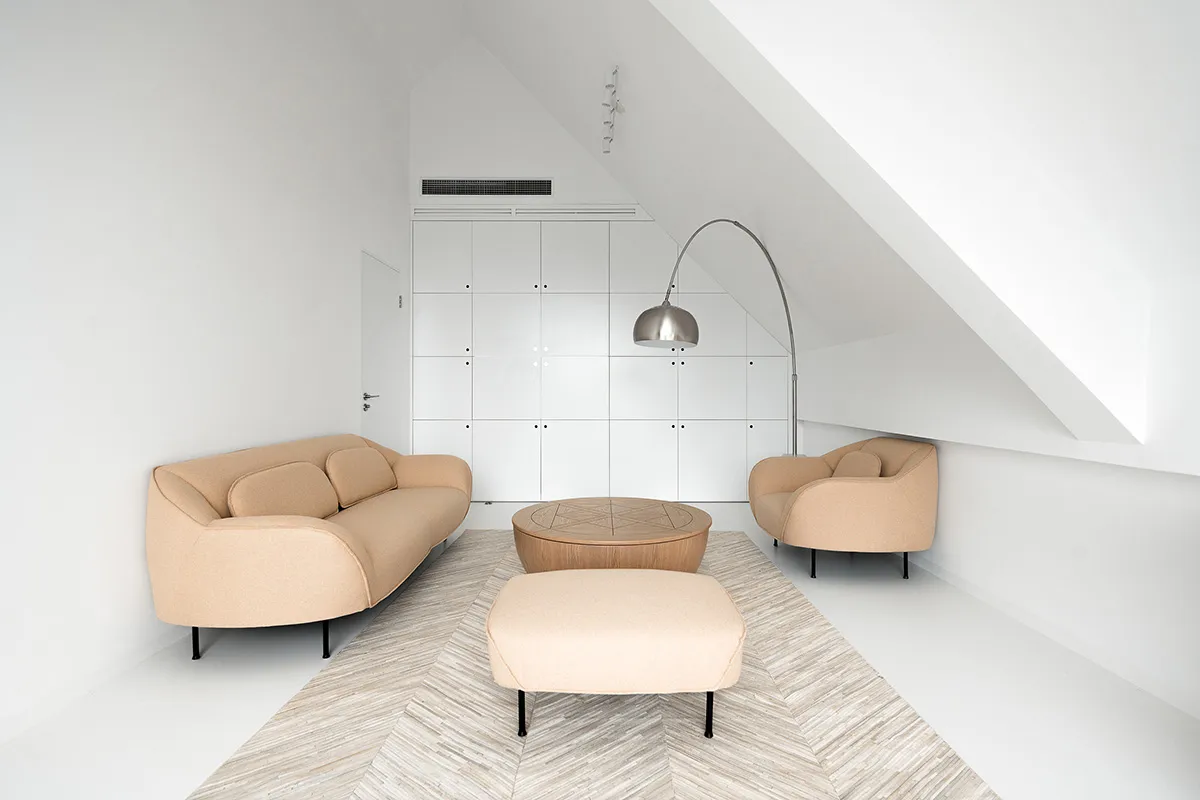 A modern minimalist living room with a beige sofa, two beige armchairs, a round wooden coffee table, and a tall floor lamp in