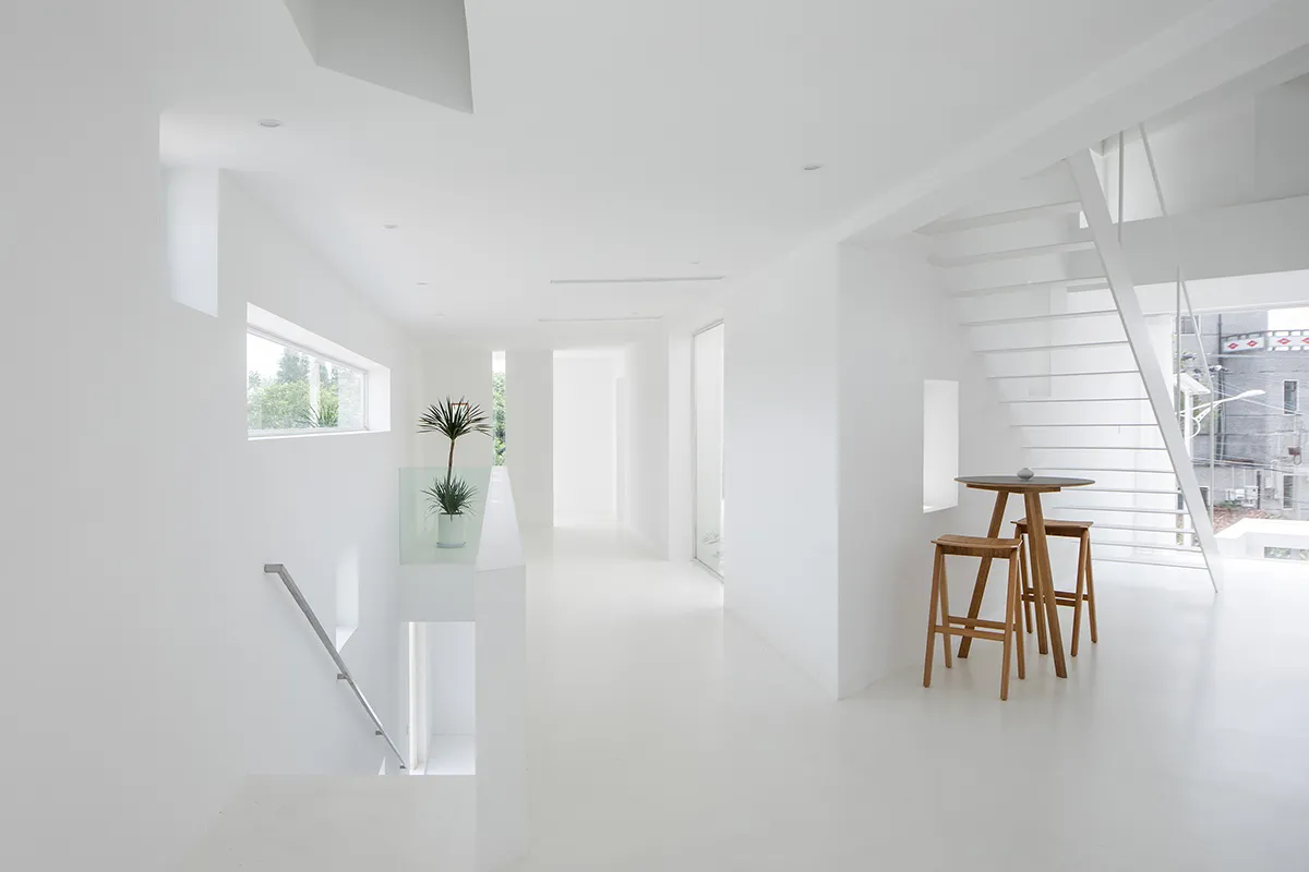 A modern white interior featuring a glass wall, metal railing, and wooden stools.