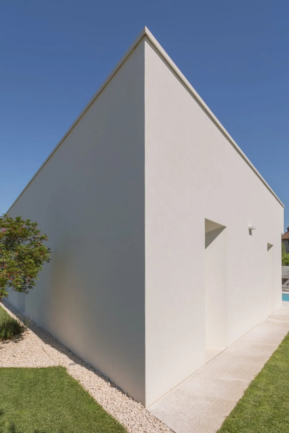 A minimalist modern house with a white stucco exterior and a triangular roof.