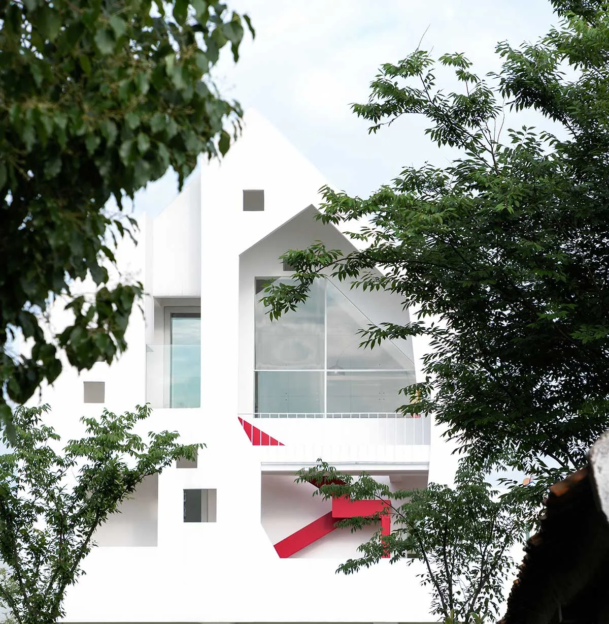 A minimalist white exterior residential house surrounded by green trees.
