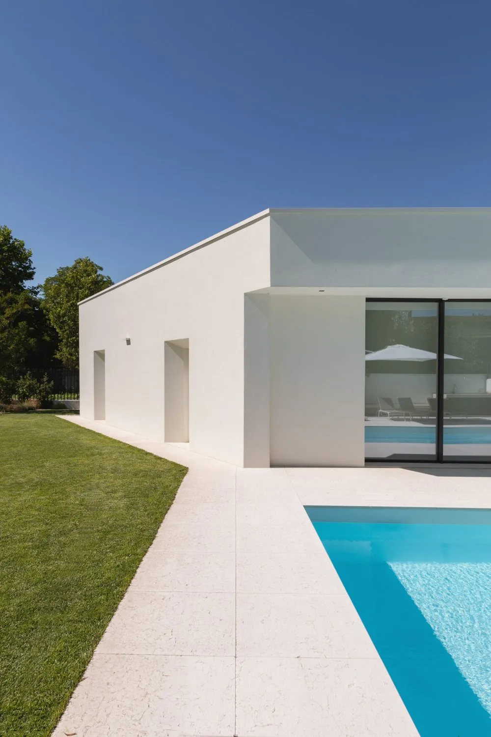 A minimalist white house with a concrete exterior and a modern swimming pool.