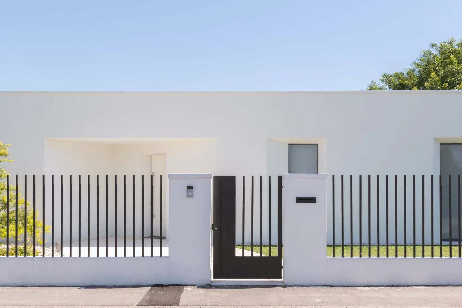 A modern house with a white exterior, concrete fence, and black metal gate.