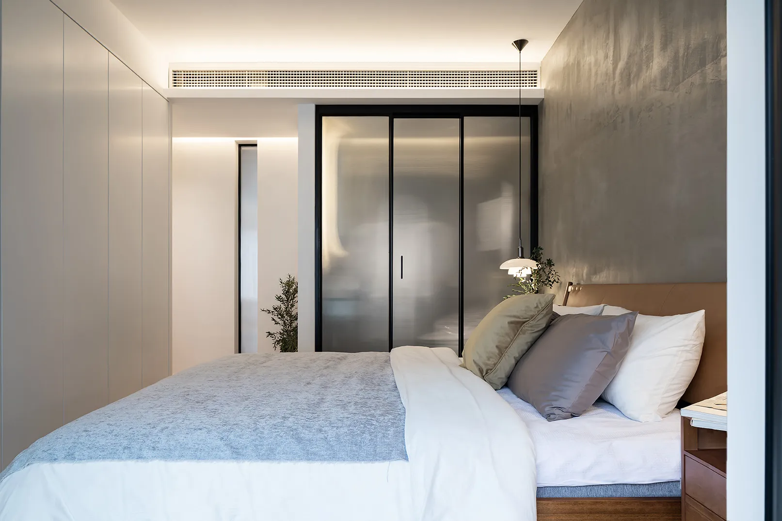 A minimalist bedroom featuring a bed with wooden frame, metal details, and a glass door wardrobe.