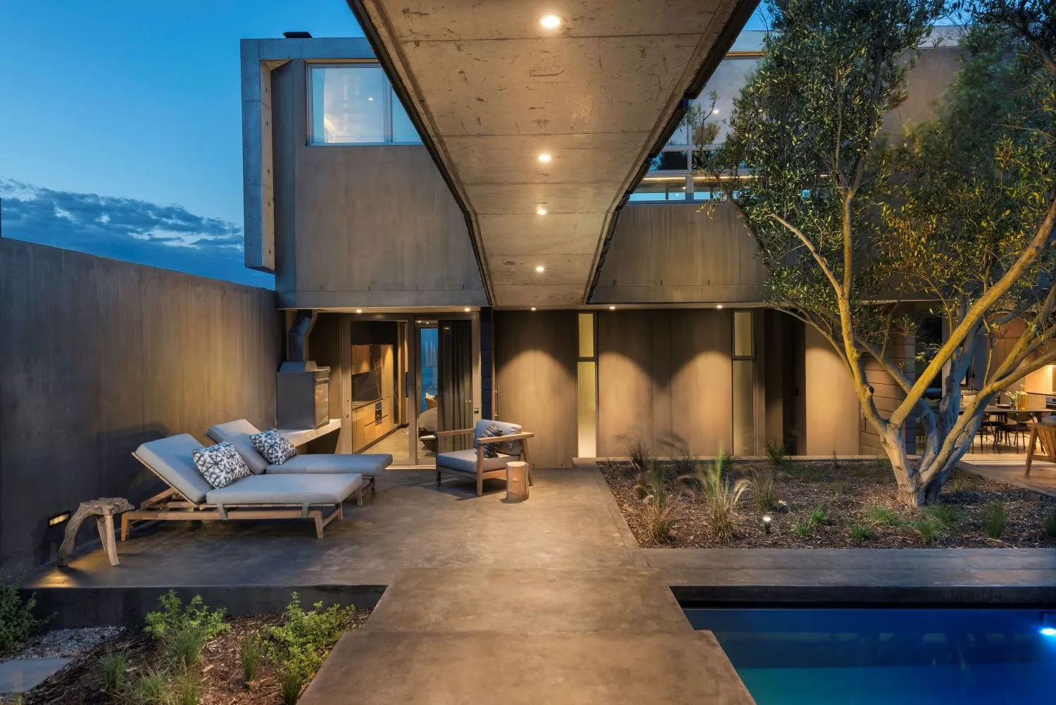 A modern residential interior with a concrete aesthetic, featuring a spacious open-plan living area with a fireplace, lounge