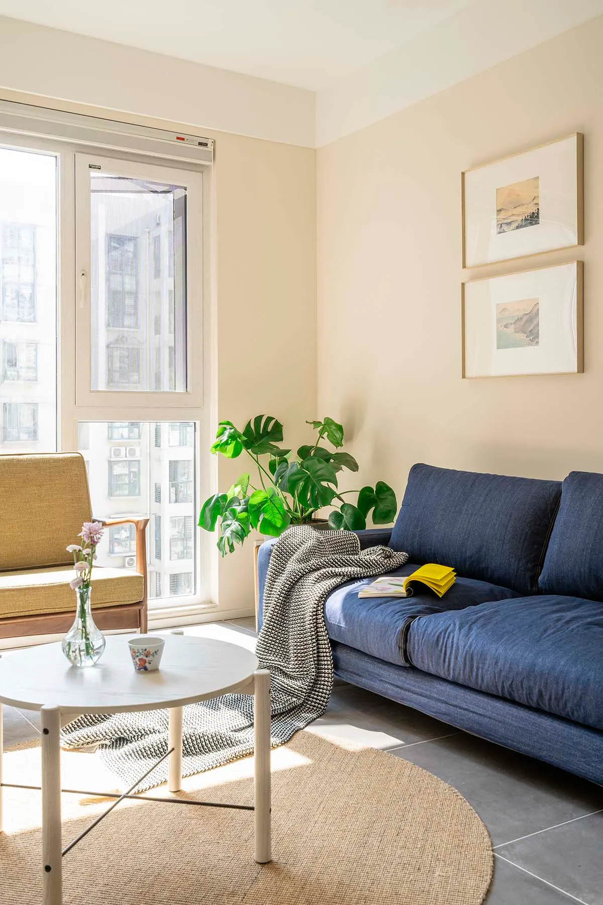 A minimalist living room with a blue sofa, green plant, and round coffee table.