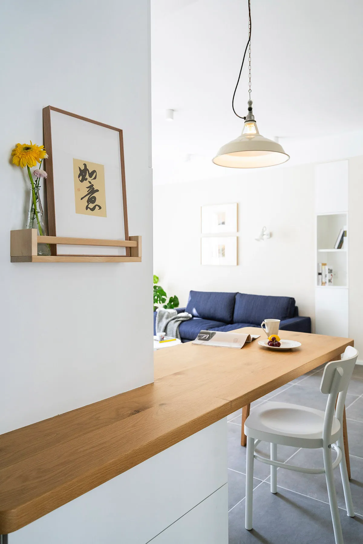 A minimalist interior with a wooden table and counter, featuring a white chair and a blue couch in the background.