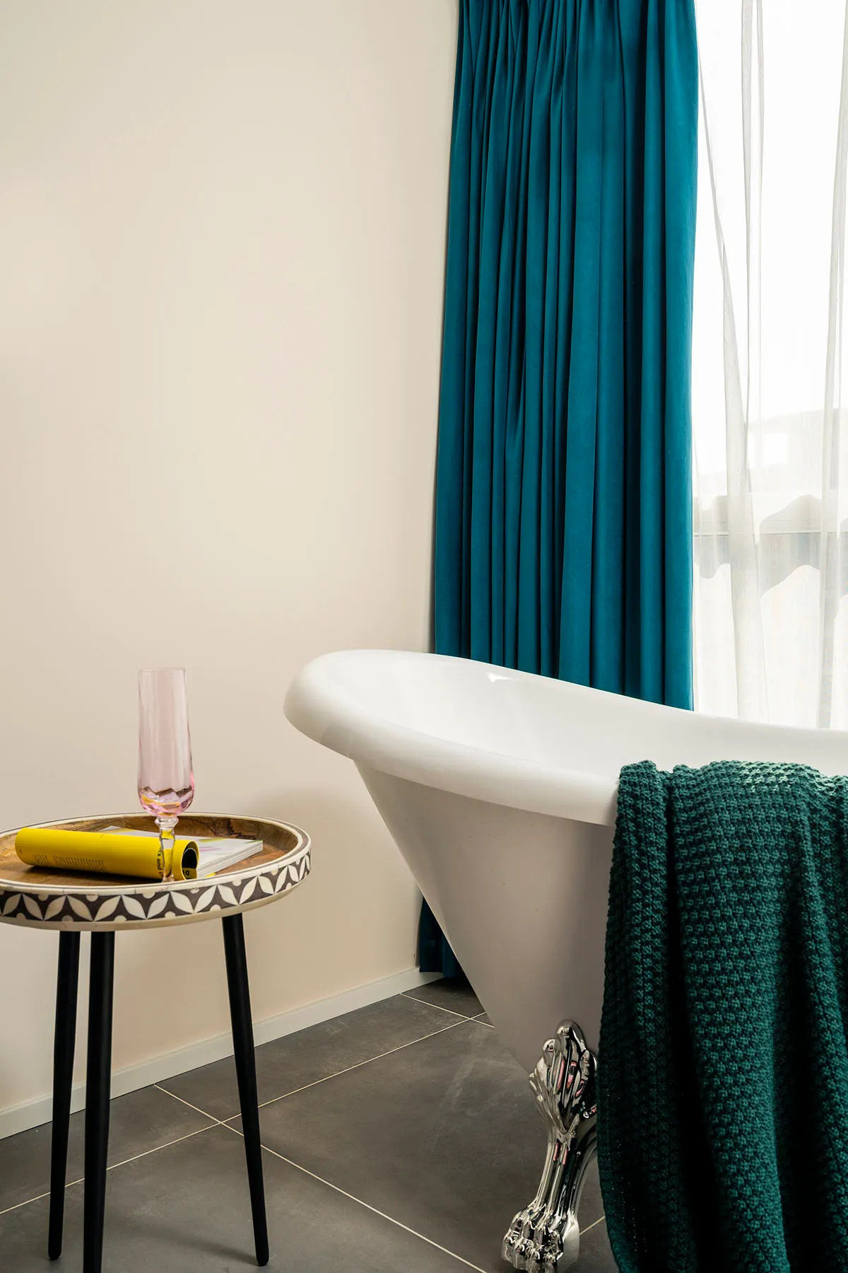 A minimalist bathroom with a white bathtub, teal curtains, and black metal legs.