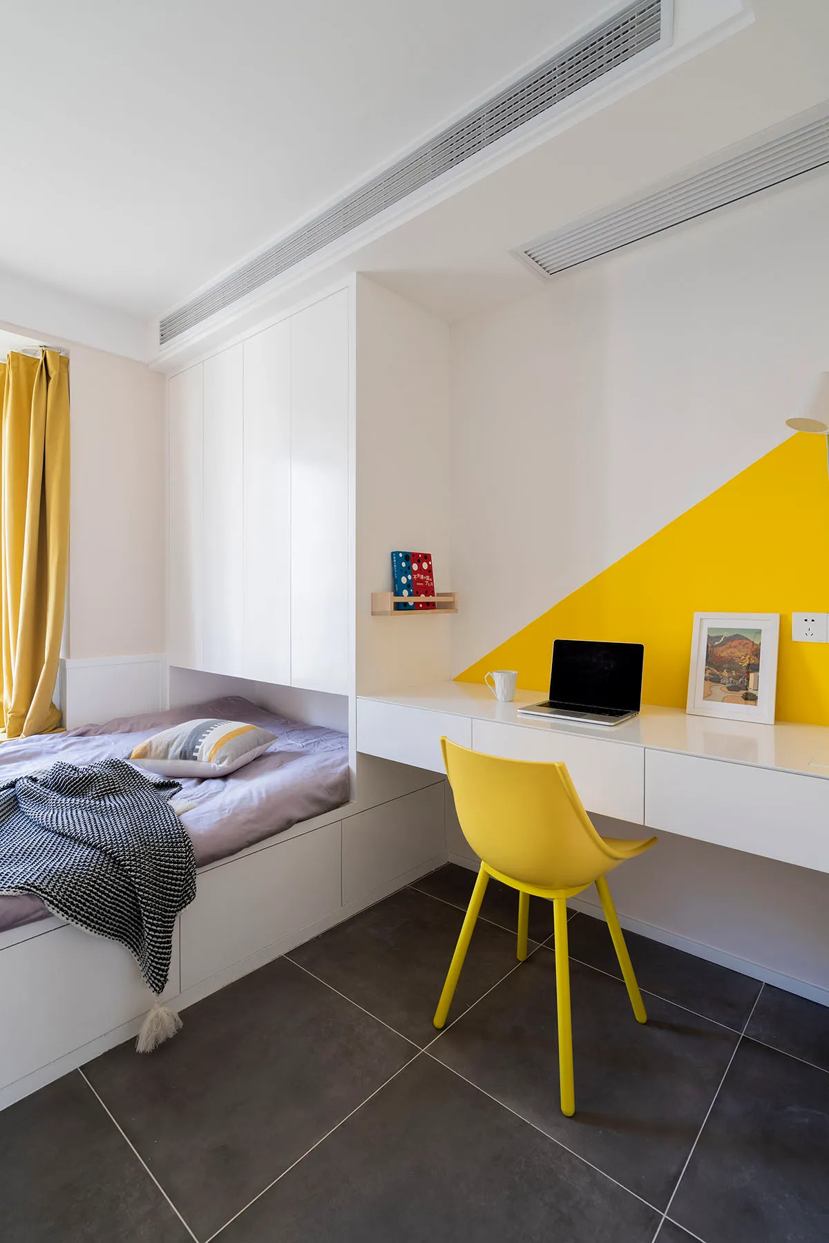 A minimalist bedroom with white furniture, yellow accents, and a built-in desk area.