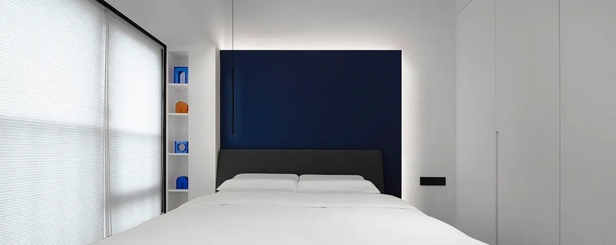 A minimalist bedroom featuring a white bed with blue accents.