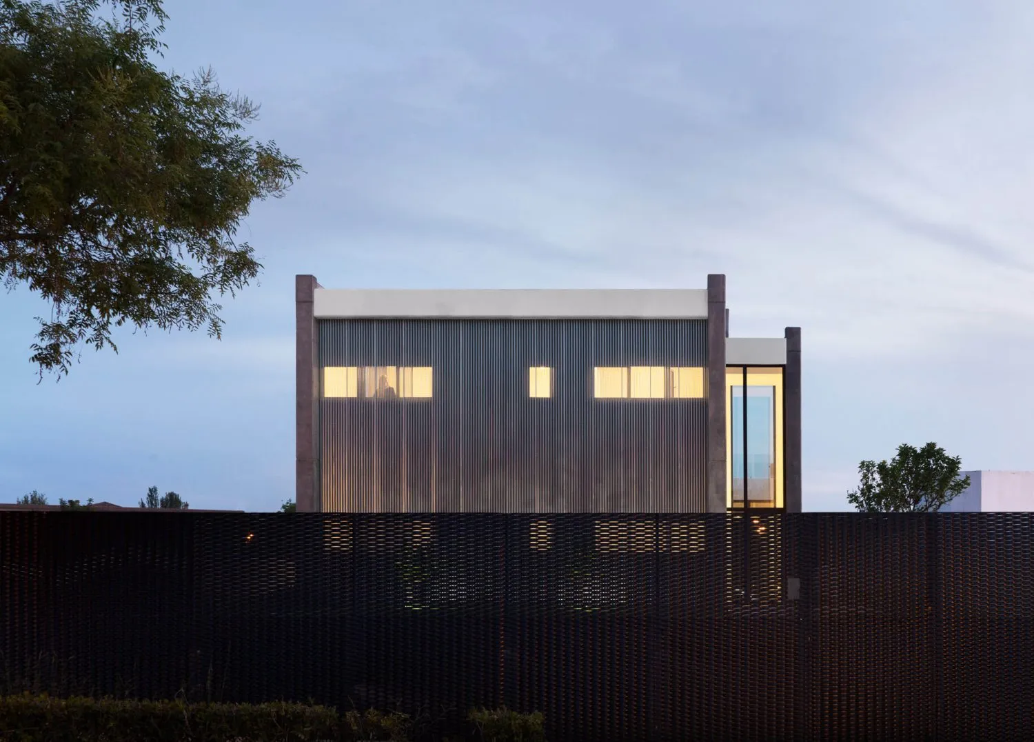 A modern architectural structure with a metallic wall, windows, and a black fence.