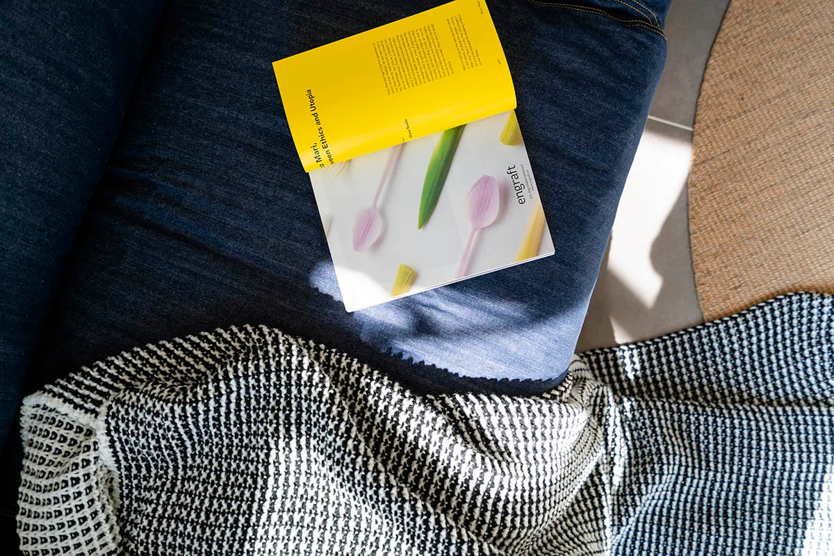 A modern living space featuring a patterned blanket draped over a footstool with a book resting on it.