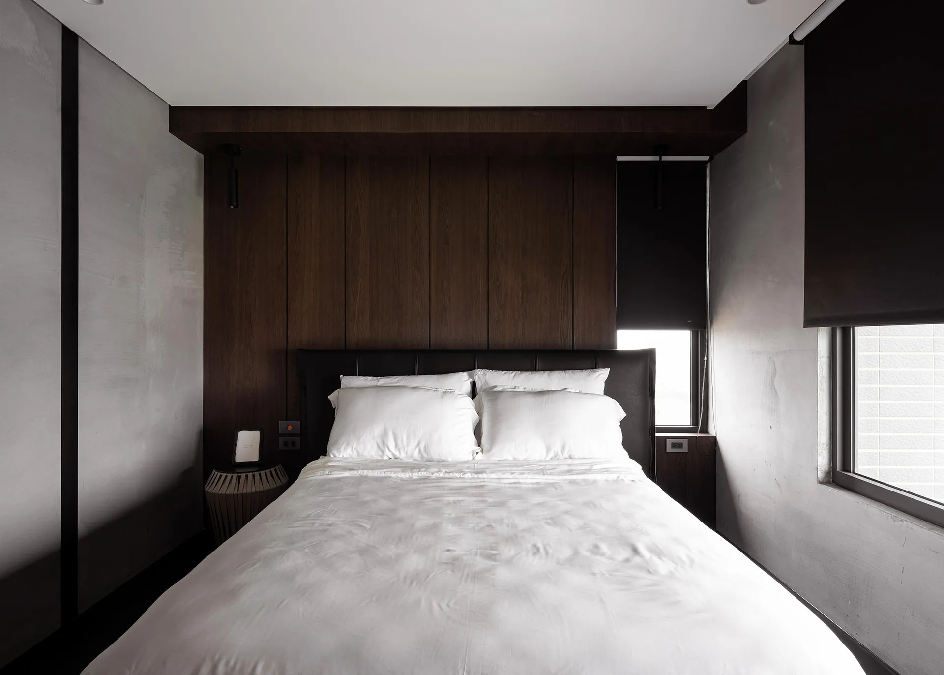 A modern minimalist bedroom with dark wood paneling and white bedding.